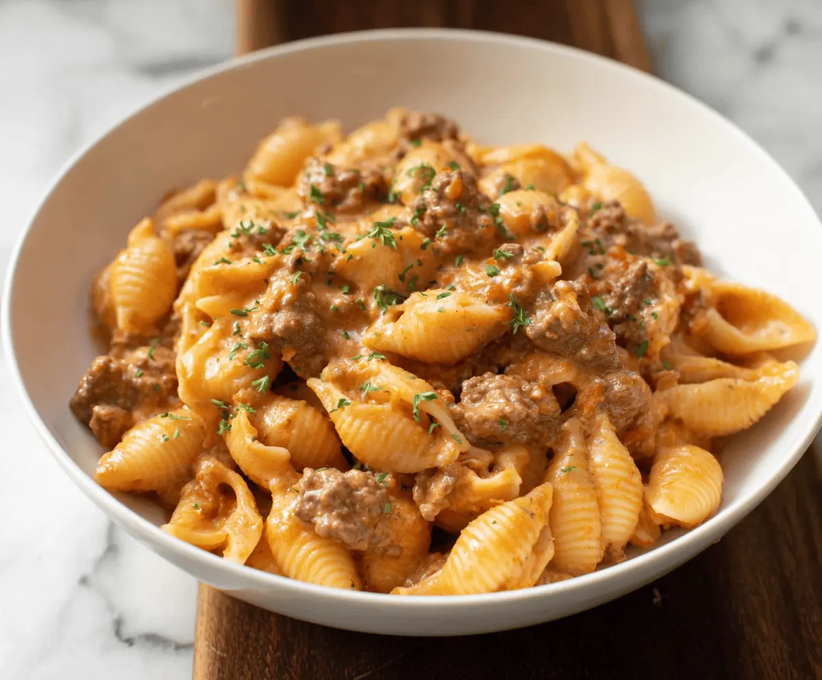 Creamy beef and shells pasta dish with melted cheese and fresh herbs on a white plate, served hot and garnished for a delicious meal
