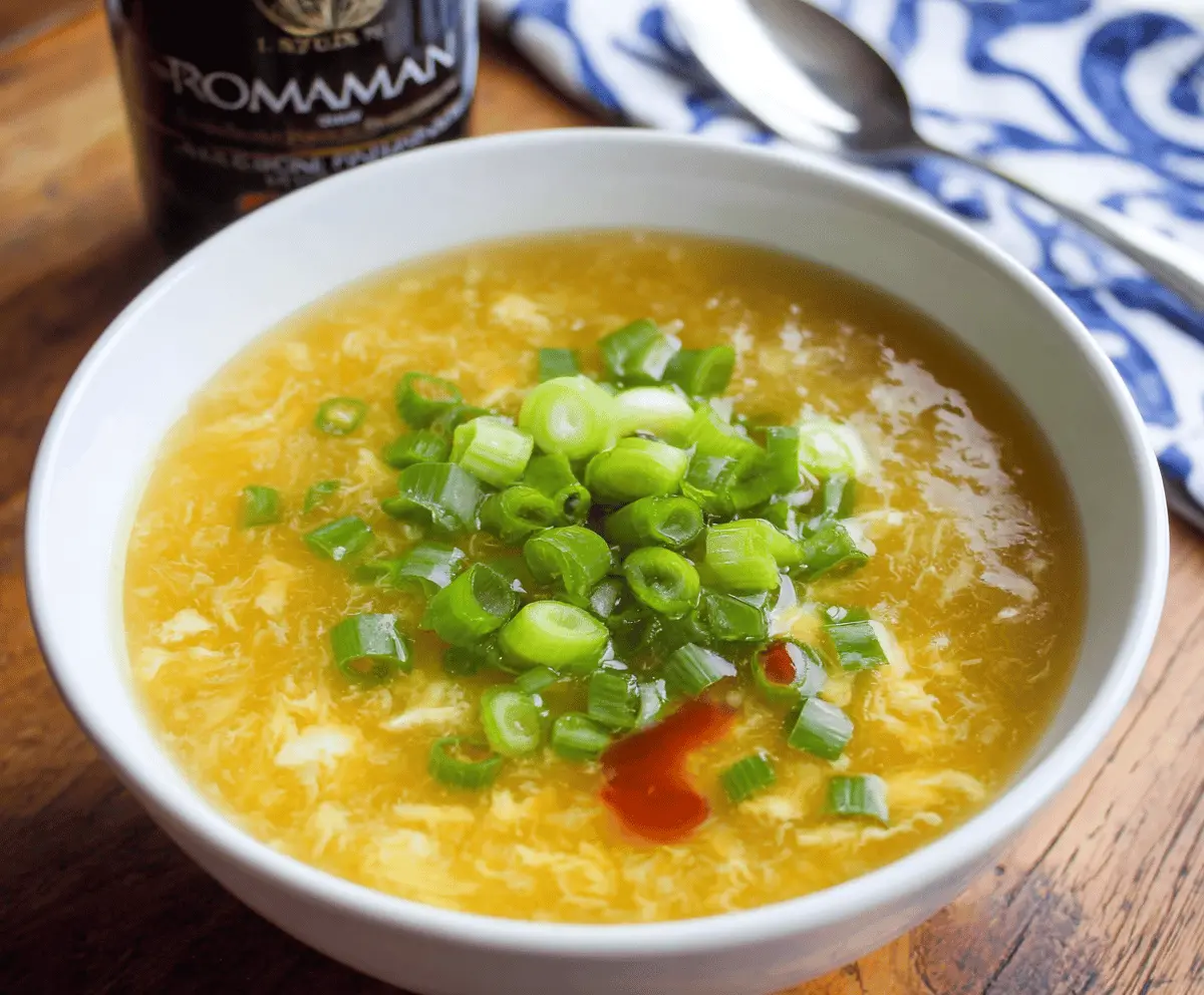 A bowl of steaming egg drop soup garnished with chopped scallions and cilantro, featuring silky egg ribbons in clear savory broth.