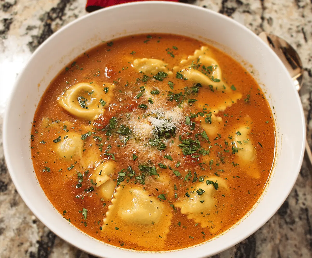 A bowl of hearty ravioli soup featuring stuffed ravioli, fresh vegetables, and herbs in a flavorful broth, served garnished with basil and grated cheese.