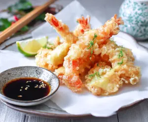 Crispy Japanese shrimp tempura served with dipping sauce on a traditional plate.