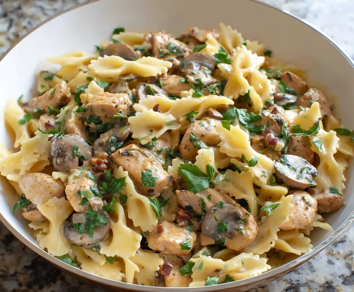 Delicious chicken mushroom pasta served on a white plate, garnished with herbs.