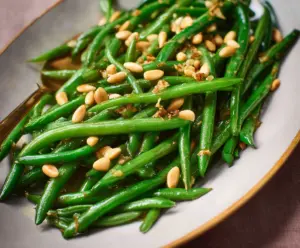 Delicious green beans with toasted pine nuts garnished with herbs, perfect for a healthy side dish.